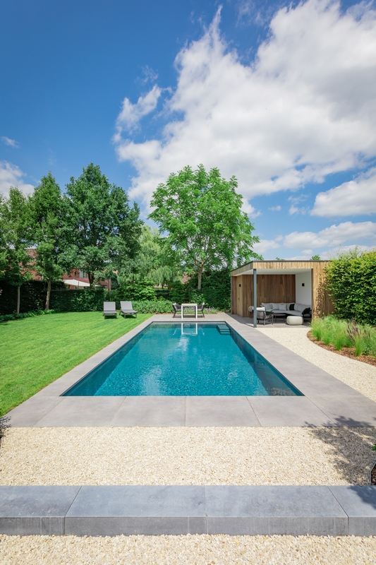 Een tuin met zwembad uit natuursteen en poolhouse.